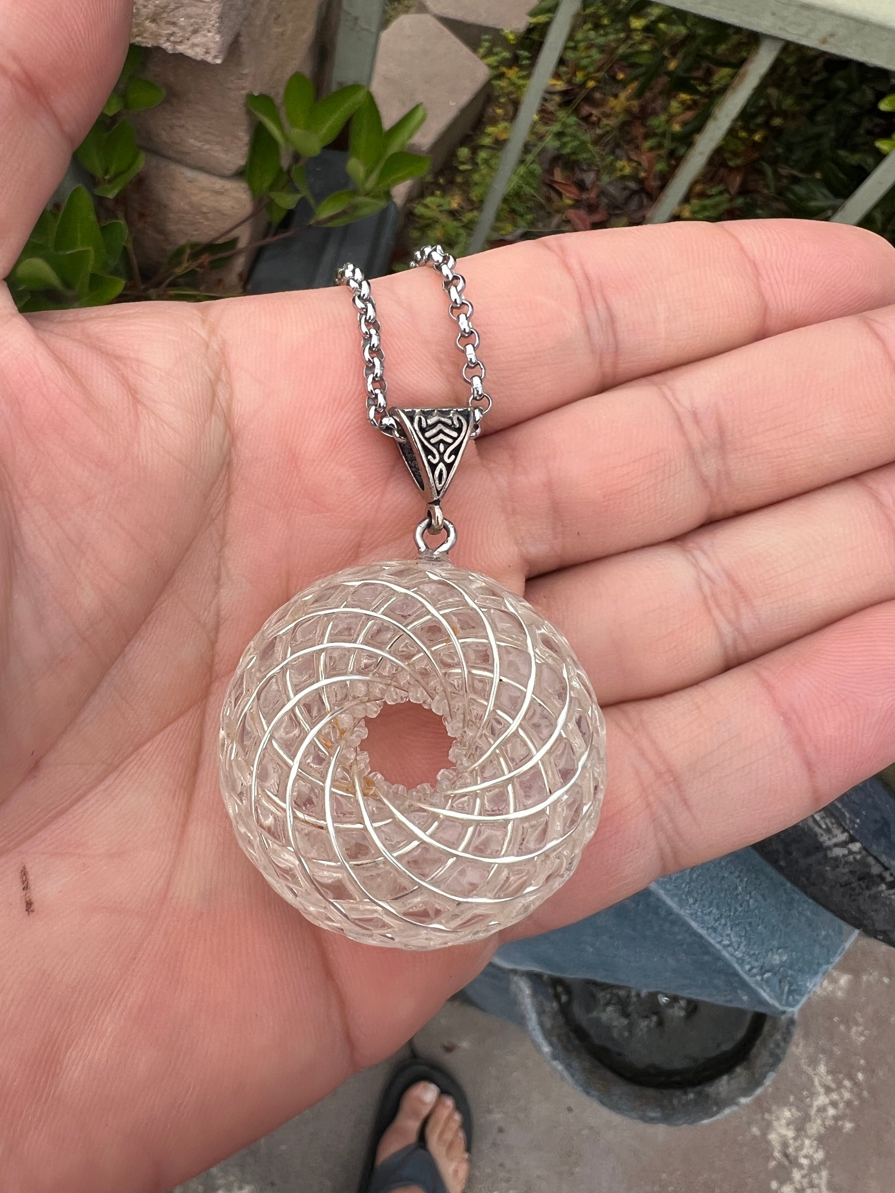 Rare rainbow phenakite jewelry pendant with intricate spiral design on silver chain held in hand